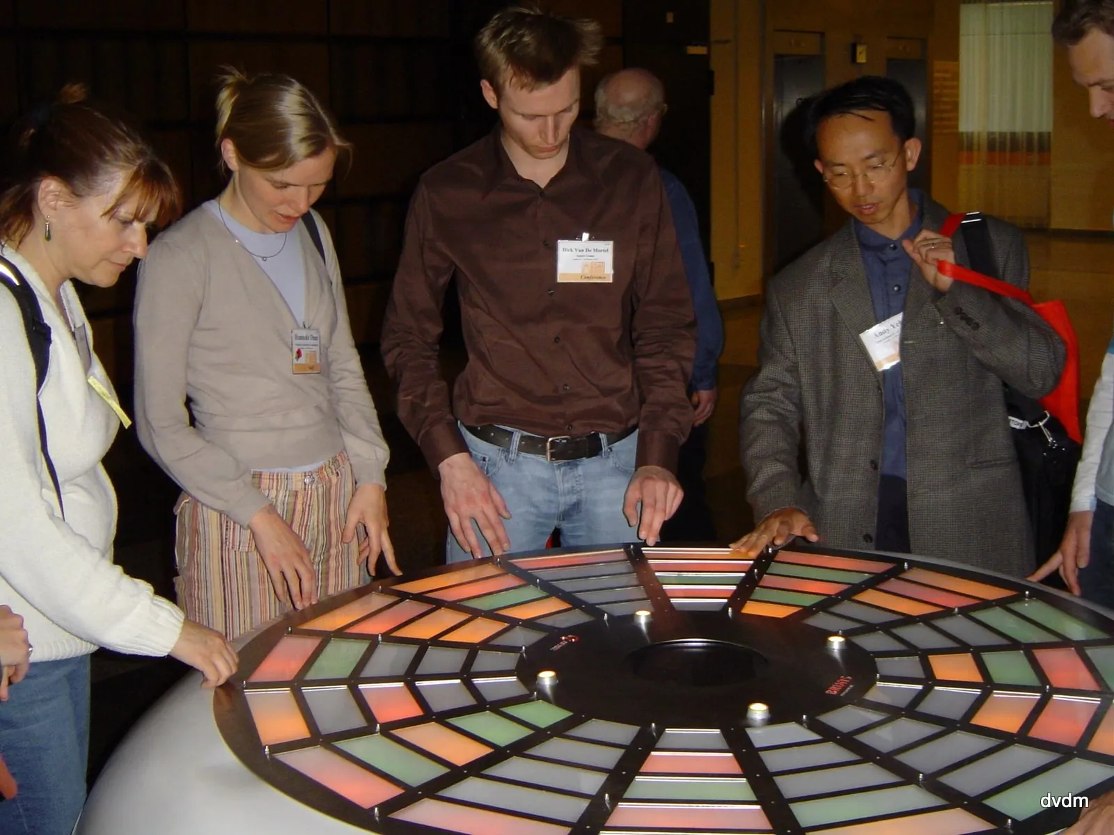CHI 2004 in Vienna: five delegates standing round the lit table with their hands resting on it, Dirk in the brown shirt, the sectors glowing amber, green and white.