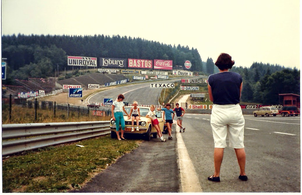 A family posing around a small car parked at the foot of Eau Rouge at
      Spa-Francorchamps in 1982, the climb behind them lined with period hoardings for Bastos,
      Gitanes, Texaco and Shell.